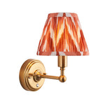 Ashstead LED wall light with orange and cream zigzag pleated fabric shade on a brushed brass arm and round backplate, white background.