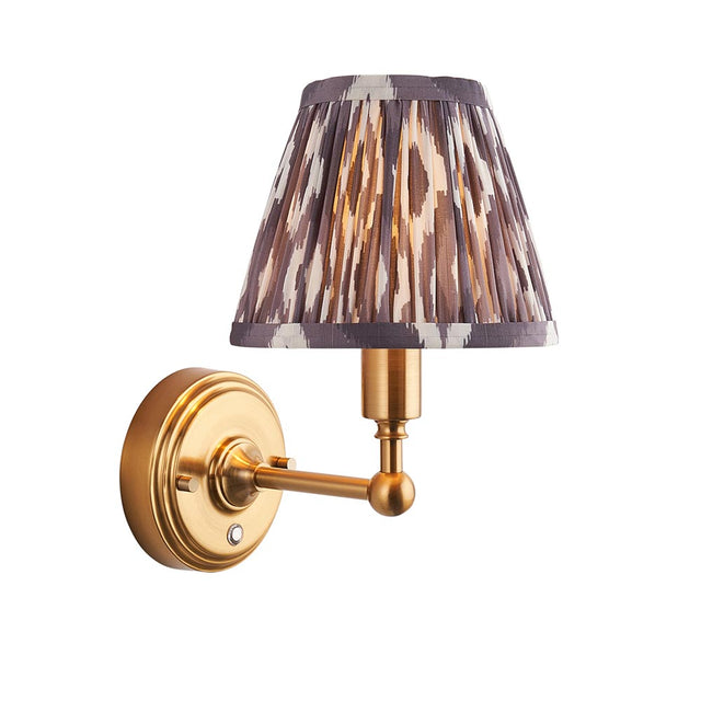 Ashstead LED Ikat wall light with a pleated grey, brown and white fabric shade on a brushed brass arm, shown against a white background.