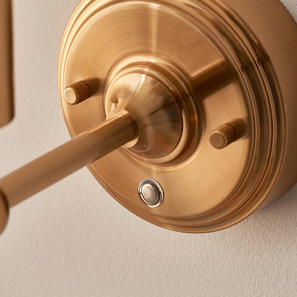 Close-up of the Ashstead LED Ikat Wall Light in brushed brass, showing the arm mount, knurled knobs and switch against a light wall.