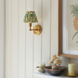Endon Ashstead LED Ikat wall light with brushed brass arm and pleated white, yellow and teal ikat shade, mounted beside a framed pineapple print.