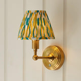 Endon Ashstead LED wall light with brushed brass arm and pleated ikat shade in yellow, jade and white, mounted on a pale panelled wall.