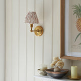 Endon Ashstead LED Ikat brushed brass wall light with pleated pink and natural fabric shade on a cream panelled wall beside a framed pineapple print.