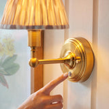 Finger tapping the touch dimmer on the brushed brass base of the Endon Ashstead LED Ikat wall light with pleated natural fabric shade.