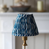 Endon Carlwood LED table lamp with brushed brass base and pleated marlin blue Ripple shade in a wavy print, shown on a mantel setting.