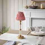 Endon Carlwood cordless LED table lamp with brushed brass base, clear acrylic detail and pink Ikat pleated shade on a dining table by a white fireplace.