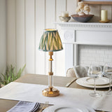 Carlwood LED Table Lamp in brushed aged brass with clear acrylic column and pleated green Zigzag shade, shown on a dining table near a white mantelpiece.