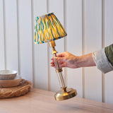 Carlwood LED table lamp with brass base, clear glass detail, and pleated yellow, teal and white Ikat shade on a wooden sideboard.