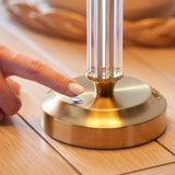 Close-up of the Carlwood LED table lamp's brass base with touch dimmer button, fluted glass column, and finger pressing to switch on.