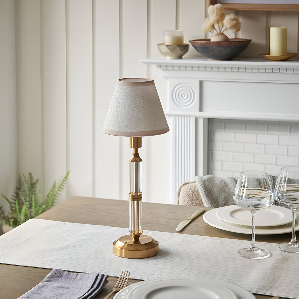Endon Carlwood LED rechargeable table lamp in brushed brass with clear acrylic stem and ivory tapered shade, styled on a set dining table.