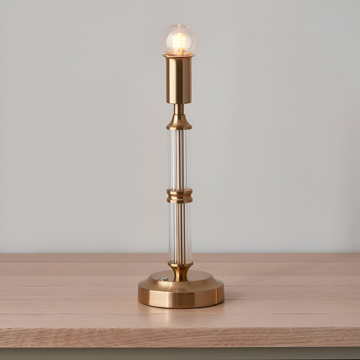 Endon Carlwood LED rechargeable table lamp in brushed brass with clear acrylic column, glowing globe bulb, shown on a wooden surface.