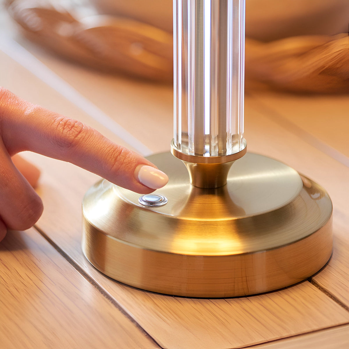 Finger pressing the touch dimmer button on the brushed brass base of the Endon Carlwood LED rechargeable table lamp on a wooden surface.