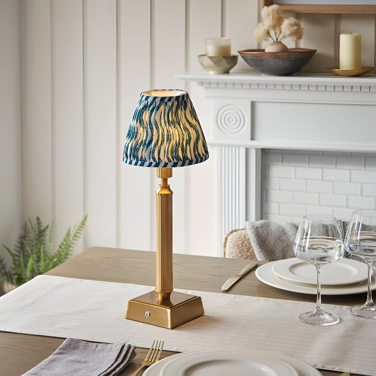 Cranwick LED rechargeable table lamp with a reeded brass stem, square base, and blue ripple-patterned fabric shade, shown on a dining table.
