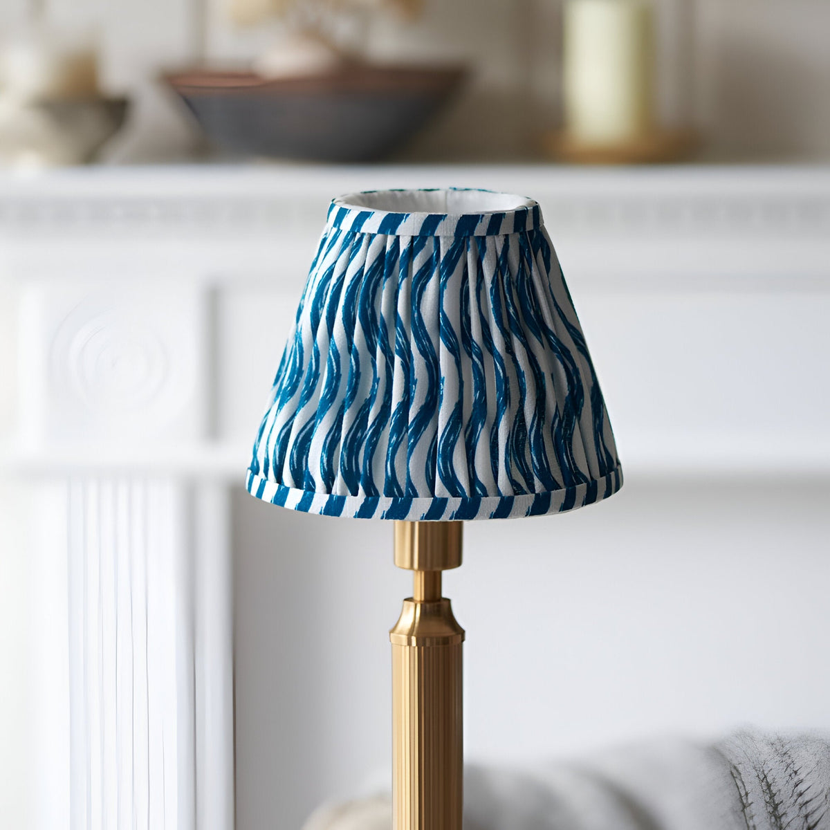 Cranwick LED rechargeable table lamp with pleated blue and white ripple-print fabric shade on a reeded brass stem, shown against a light interior backdrop.