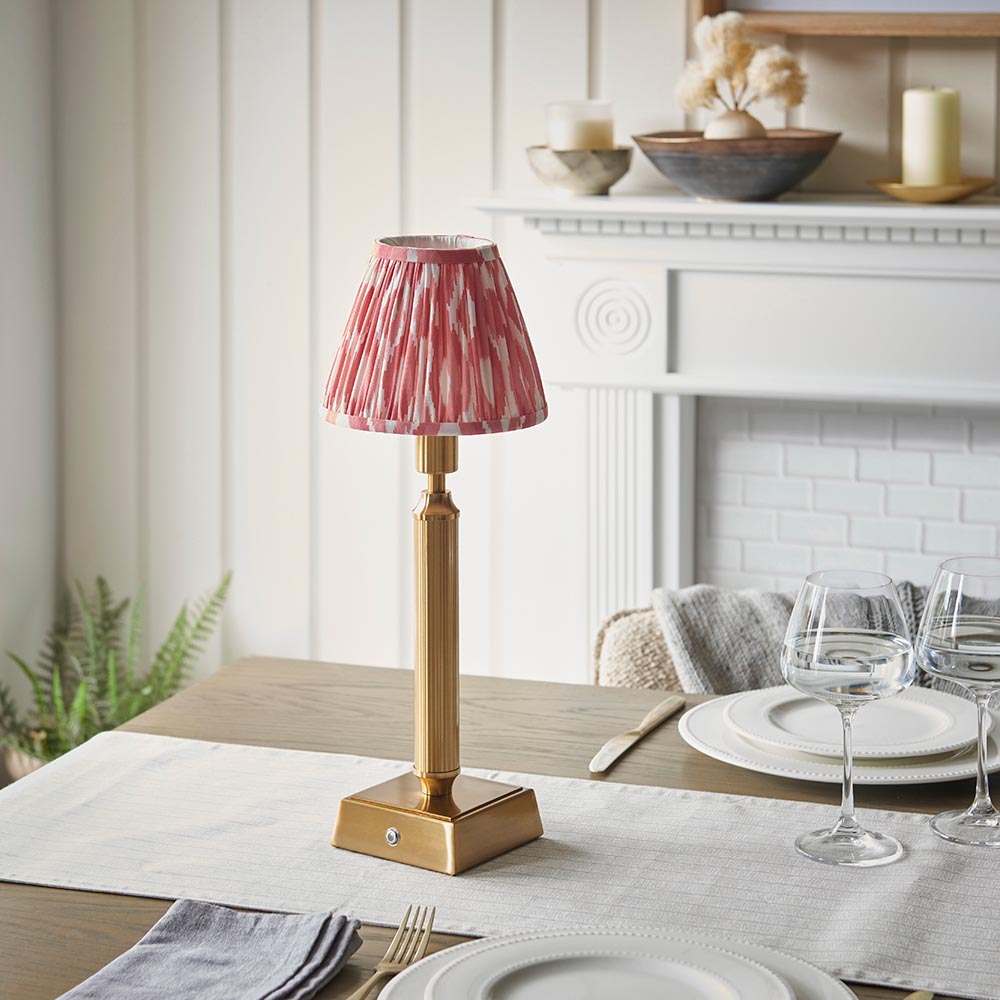 Endon Cranwick LED Ikat table lamp with brushed brass reeded stem and pink and white ikat shade, on a dining table set with wine glasses.
