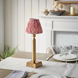 Endon Cranwick LED Ikat table lamp with brushed brass reeded stem and pink and white ikat shade, on a dining table set with wine glasses.