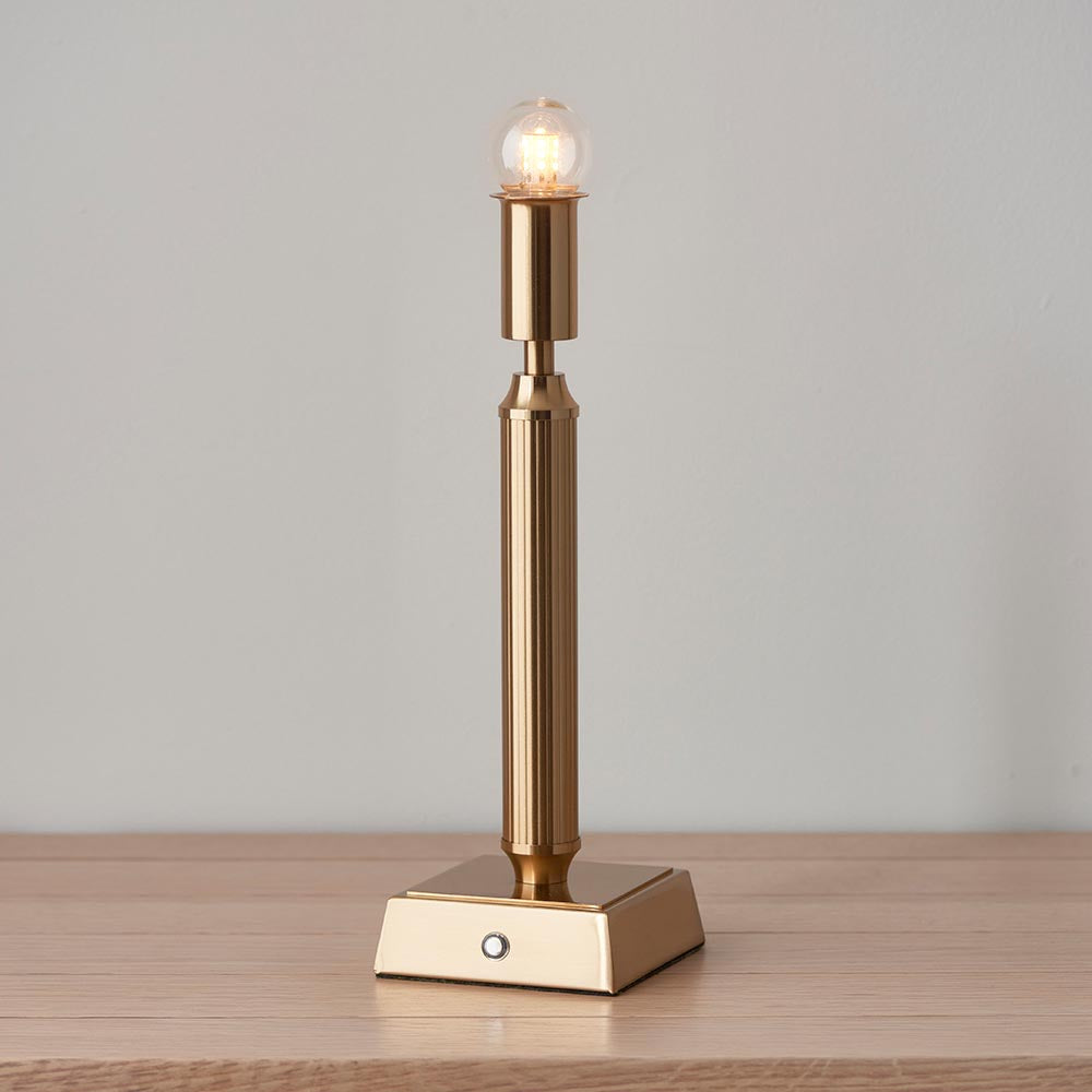 Endon Cranwick LED table lamp with a brushed brass reeded stem and square base, lit bulb visible without shade, shown on a wooden surface.