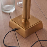 Close-up of the Endon Cranwick Ikat table lamp base, showing the reeded brushed brass stem, square plinth, and USB-C charging cable connected.