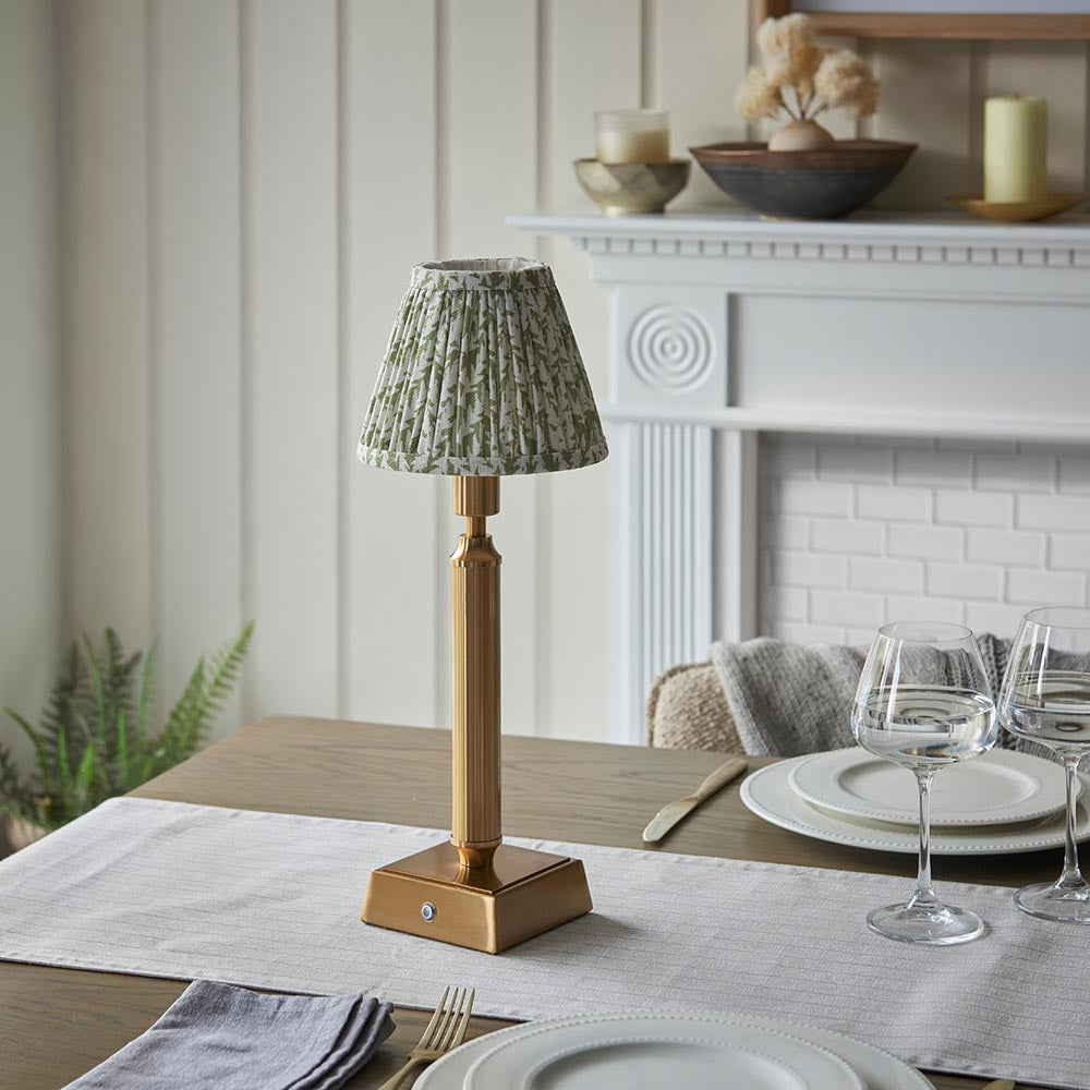 Endon Cranwick LED Leaf table lamp with brushed brass reeded stem and green leaf-print pleated shade, styled on a dining table beside wine glasses.