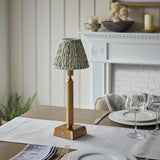 Endon Cranwick LED Leaf table lamp with brushed brass reeded stem and green leaf-print pleated shade, styled on a dining table beside wine glasses.