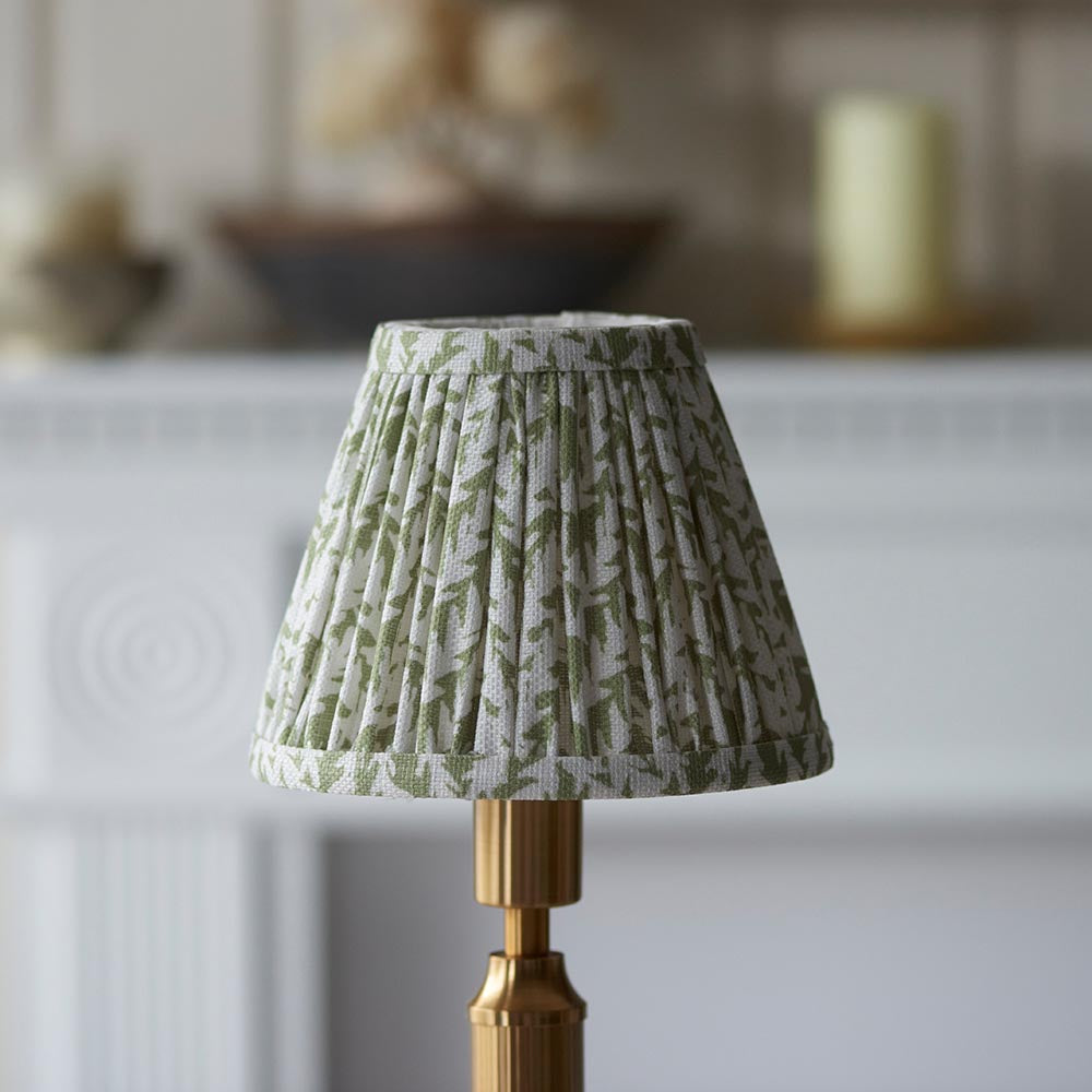 Endon Cranwick LED Leaf table lamp with pleated green and white leaf-print shade on a brushed brass stem, shown on a pale mantelpiece setting.