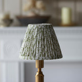 Endon Cranwick LED Leaf table lamp with pleated green and white leaf-print shade on a brushed brass stem, shown on a pale mantelpiece setting.