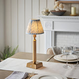 Endon Cranwick LED table lamp with brushed brass reeded stem and blue leaf-print pleated shade, on a dining table beside wine glasses and a white fireplace.