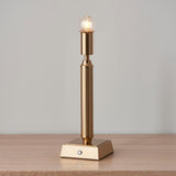 Cranwick LED table lamp with reeded brass stem, square base, exposed globe bulb, and touch control, shown on a wooden surface.