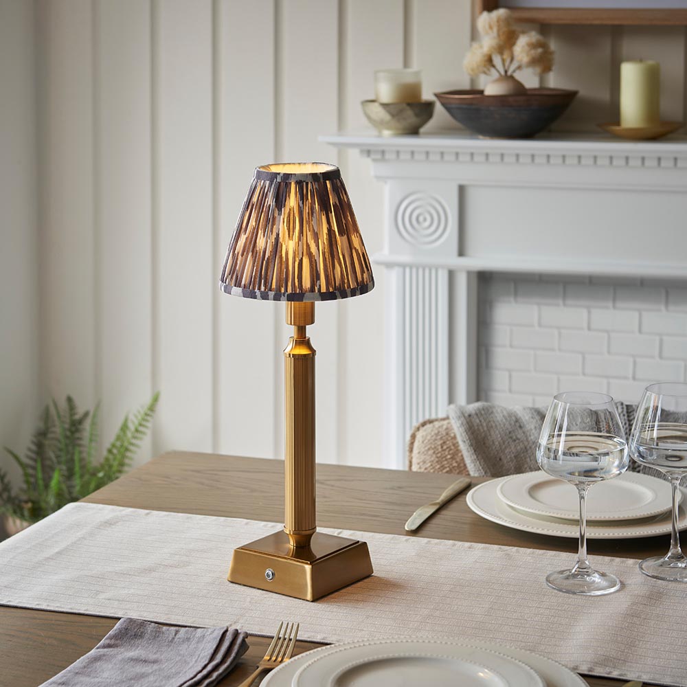 Endon Cranwick LED Ikat Table Lamp in brushed brass with reeded stem, square base and grey and white patterned clip-on shade on a dining table.