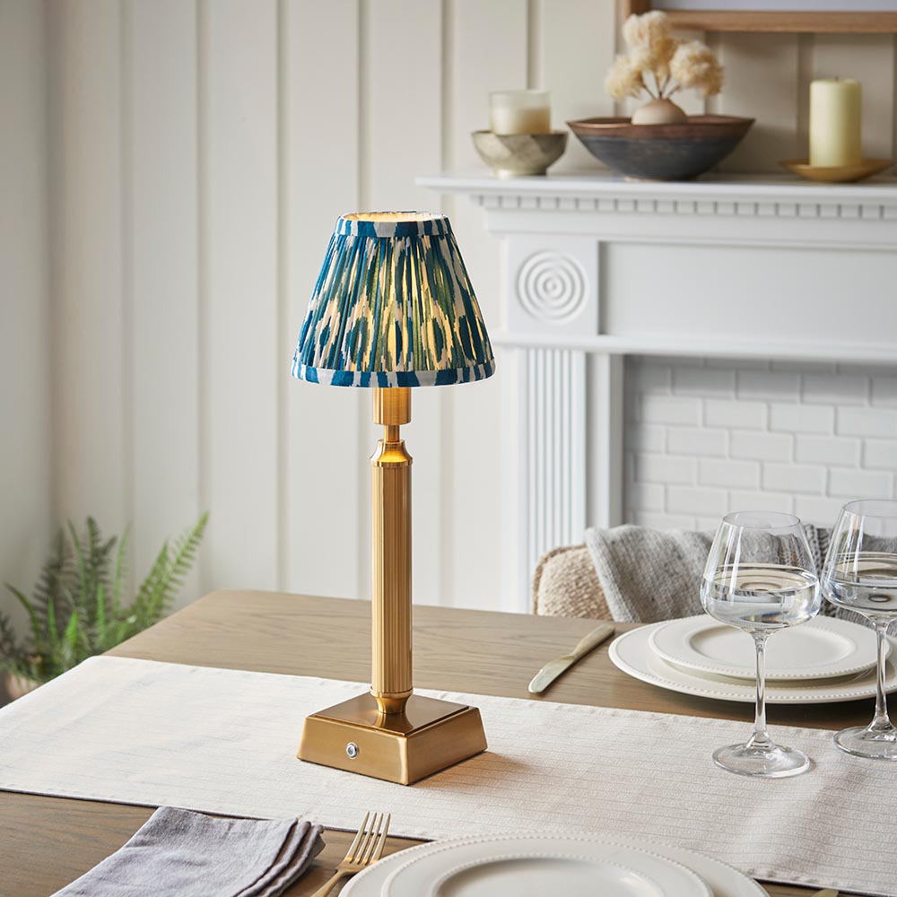 Cranwick LED Ikat Table Lamp with brass reeded stem, square base and blue-and-white patterned fabric shade, shown on a dining table setting.
