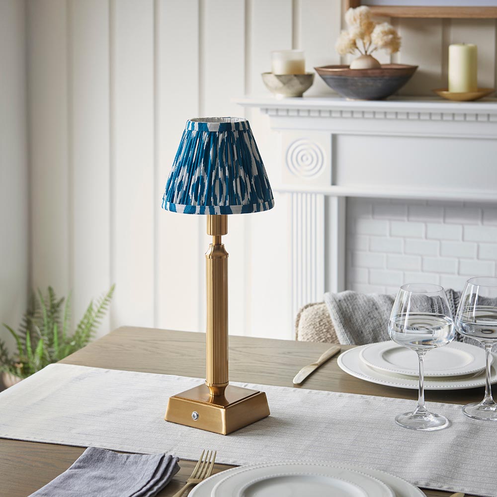 Cranwick LED Ikat rechargeable table lamp with brass reeded stem, square base and blue-white patterned shade, shown on a dining table.
