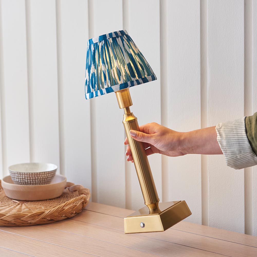 Cranwick LED Ikat Table Lamp with brass reeded stem, square base and blue patterned fabric shade, held by hand in a room setting.