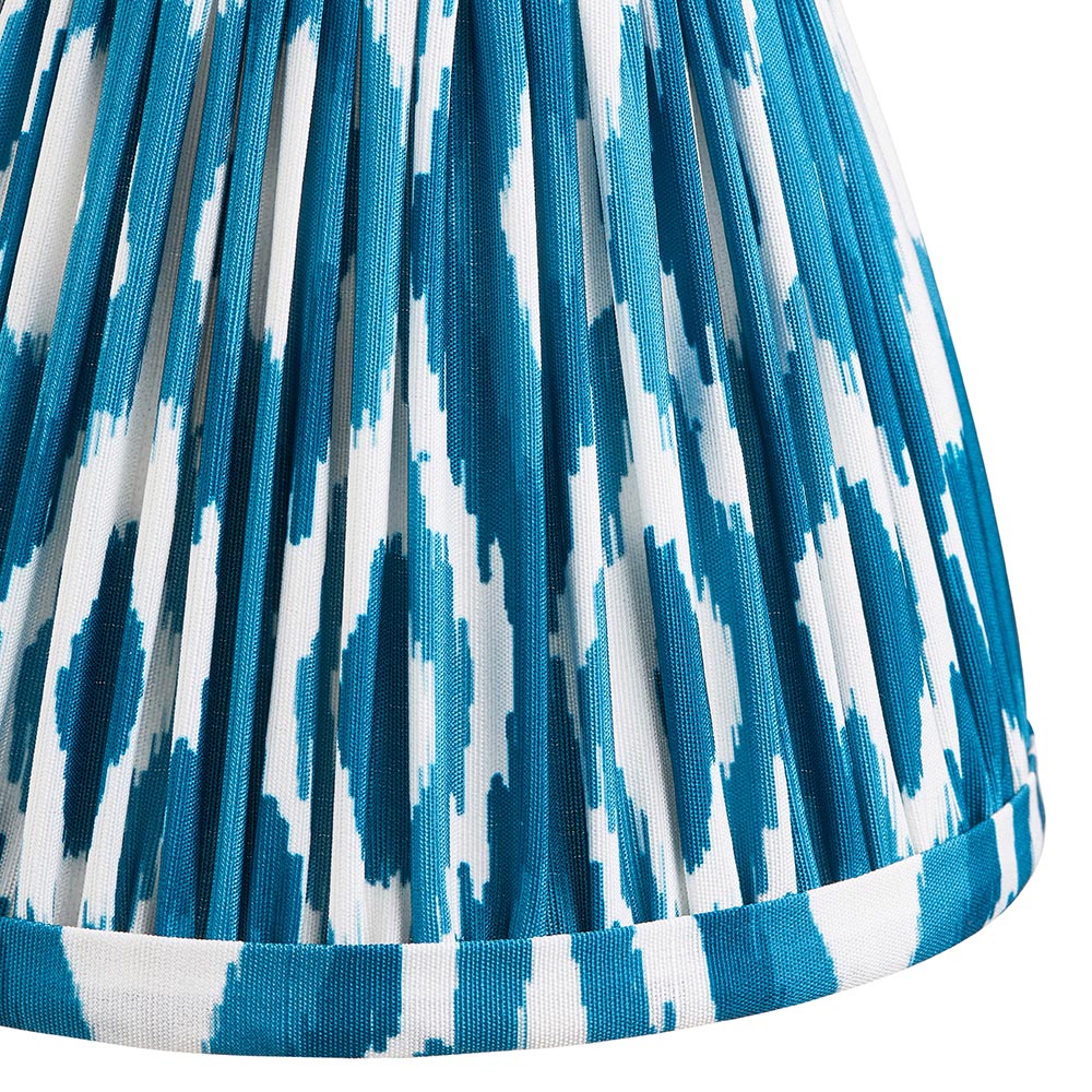 Close-up of the Cranwick LED Ikat Table Lamp's pleated shade, showing blue and white ikat-print faux silk fabric with a brass trim edge.