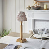 Cranwick LED Ikat Table Lamp with brass reeded stem, square base and patterned fabric shade, shown on a dining table near a white fireplace.