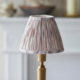 Cranwick LED Ikat Table Lamp with pleated pink and white patterned shade on a brass reeded stem, shown on a mantelpiece setting.