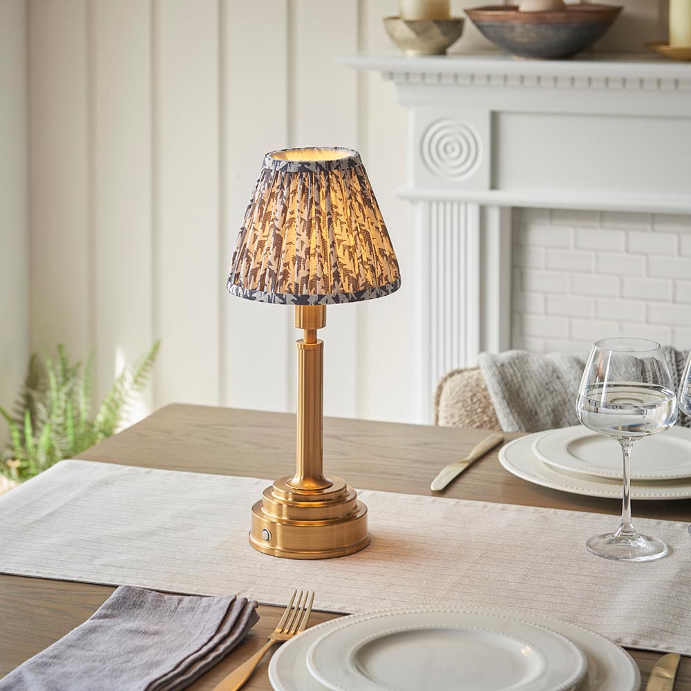 Endon Danebourne LED Leaf table lamp with brushed brass stepped base and grey and white leaf-print pleated shade, set on a dining table.
