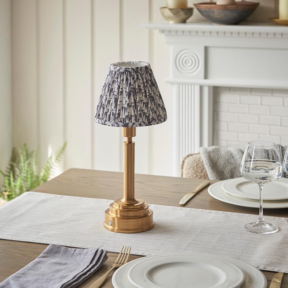Endon Danebourne LED Leaf table lamp with brushed brass stepped base and pleated grey leaf-print shade, styled on a dining table setting.
