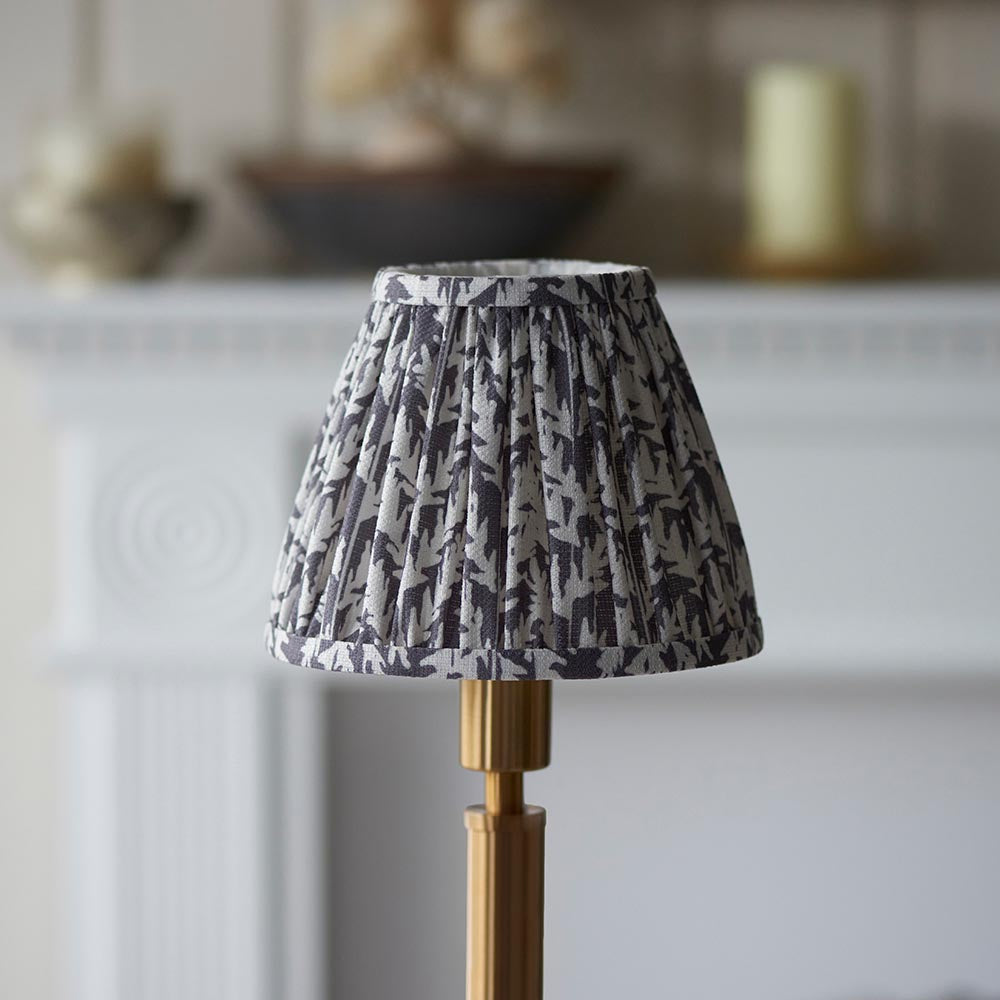 Endon Danebourne LED Leaf table lamp with a pleated grey and white leaf-print shade on a brushed brass stepped base, set before a pale fireplace.