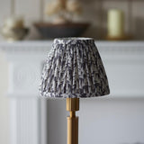 Endon Danebourne LED Leaf table lamp with a pleated grey and white leaf-print shade on a brushed brass stepped base, set before a pale fireplace.
