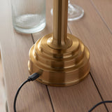 Close-up of the brushed brass stepped base of the Endon Danebourne LED Ikat table lamp on a wooden table, with USB-C charging cable connected.