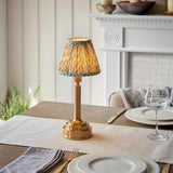 Endon Danebourne LED Leaf table lamp with brushed brass stepped base and green leaf-print pleated shade, lit on a dining table beside wine glasses.