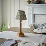 Endon Danebourne LED table lamp with brushed brass stepped base and green leaf-print pleated fabric shade, styled on a dining table setting.