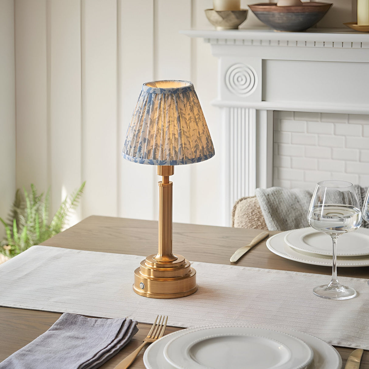 Danebourne LED Leaf Table Lamp in brass with pleated blue and white leaf-print shade, styled on a dining table beside a white fireplace mantel.