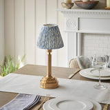 Danebourne LED Leaf Table Lamp in brass with a pleated blue and white leaf-print fabric shade, shown on a dining table near a white fireplace mantel.