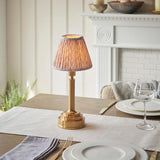 Danebourne LED Leaf Table Lamp in brass with a pleated leaf-print shade, styled on a dining table beside a white fireplace mantel.