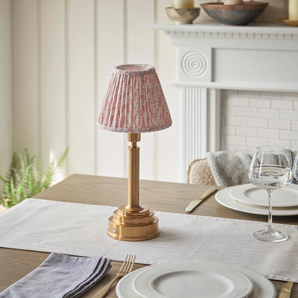 Danebourne LED Leaf table lamp in brass with a pink patterned pleated fabric shade, shown on a dining table with a touch dimmer base.