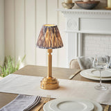 Endon Danebourne LED Ikat table lamp with brushed brass stepped base and grey pleated faux silk shade, lit on a dining table beside wine glasses.