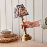 Hand adjusting the Endon Danebourne LED Ikat table lamp with brushed brass stepped base and grey and white Ikat clip-on shade on a wooden sideboard.