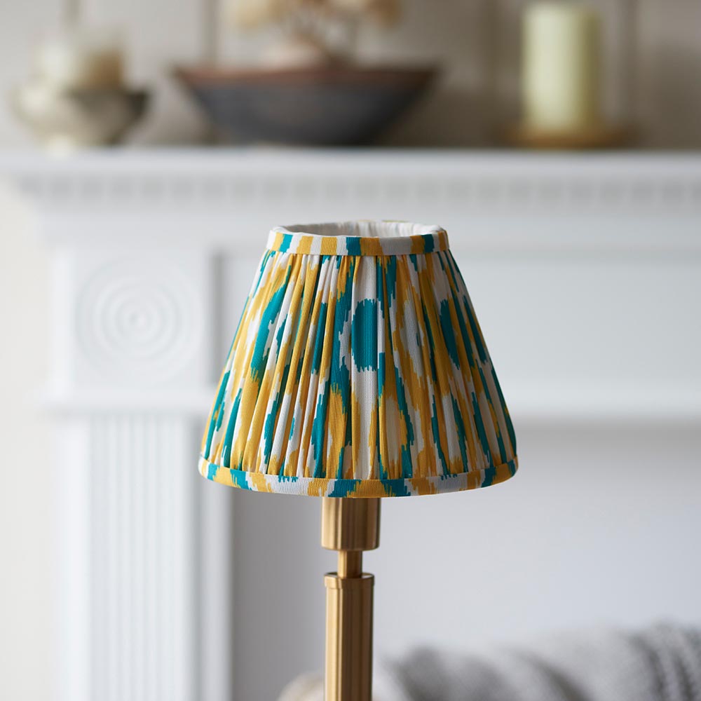 Endon Danebourne LED Ikat table lamp with brushed brass stepped base and pleated yellow, teal and white ikat shade, on a mantel setting.