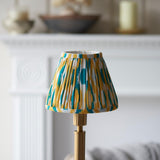 Endon Danebourne LED Ikat table lamp with brushed brass stepped base and pleated yellow, teal and white ikat shade, on a mantel setting.