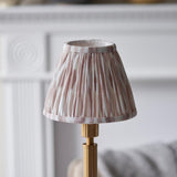 Danebourne LED Ikat Table Lamp with brushed brass stepped base and pleated pink, white and natural fabric shade, shown against a soft neutral interior backdrop.
